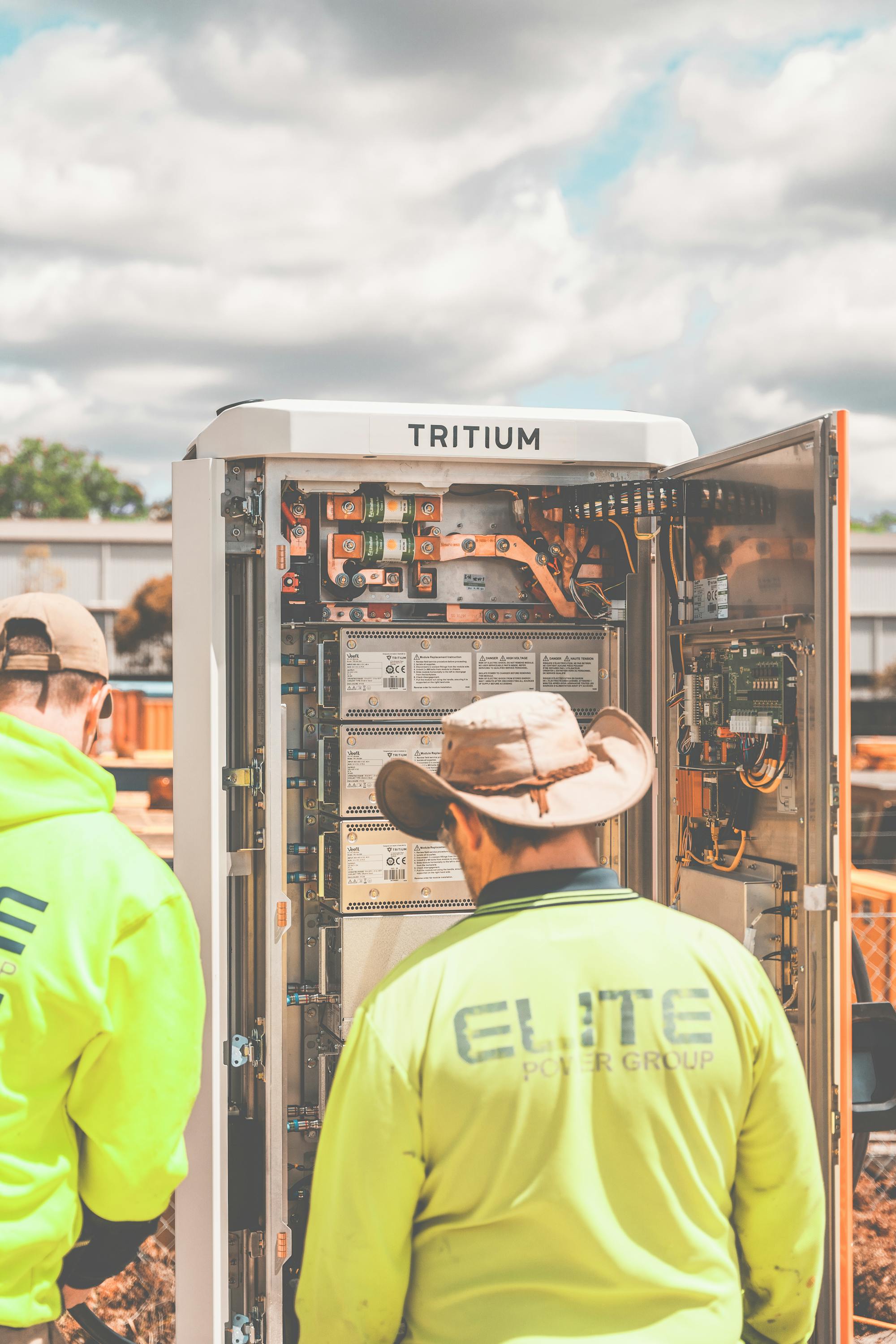 Two technicians in high-visibility vests installing a DC fast charger