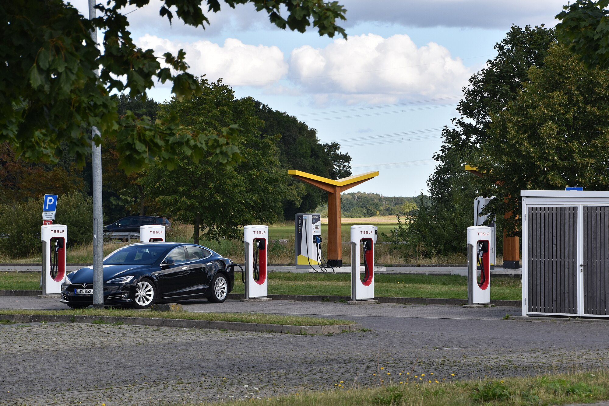Row of Tesla Superchargers alongside Fastned fast-charging stations with solar canopy at a German highway stop